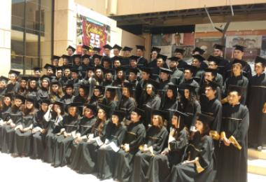 Large graduating class in black caps and gowns, many smiling, posed on outdoor steps